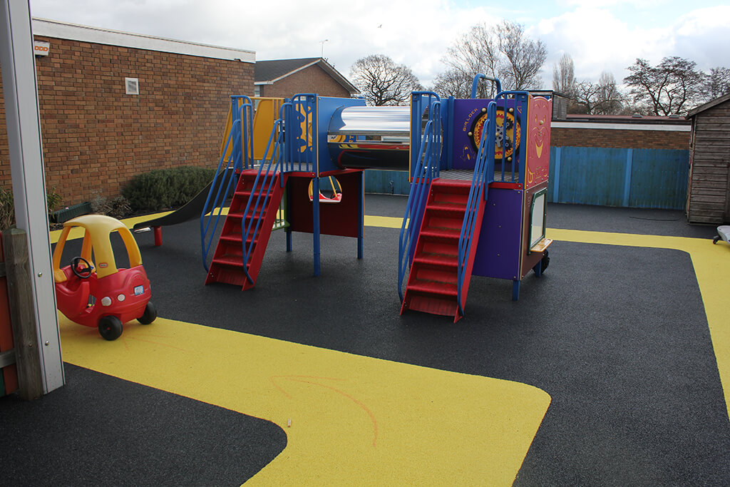 Vibrant yellow track around playground equipment with black safety surfacing. A racing track for children's car toys