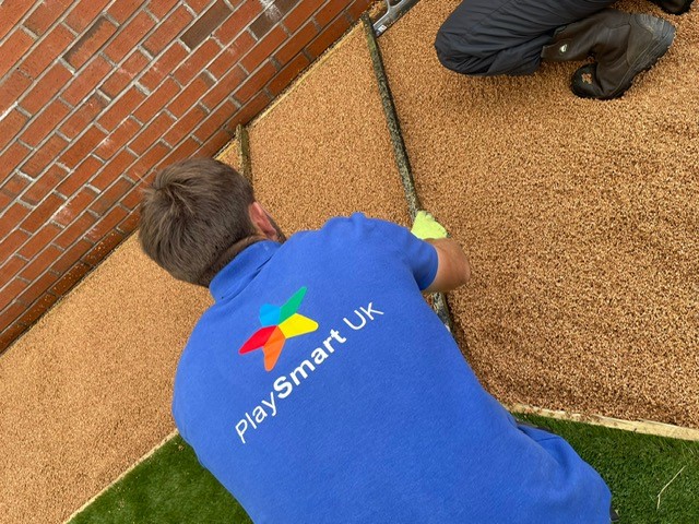 A PlaySmart installer wearing a PlaySmart branded blue shirt installs and levels a Corkeen pathway