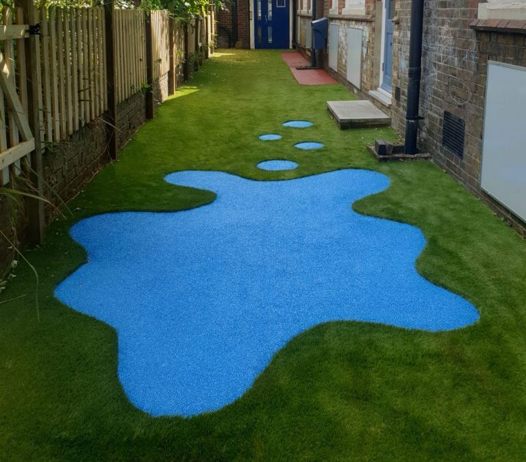 Artificial grass with bright blue wetpour surface shaped like splashed paint in the centre