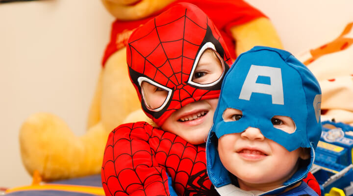 two children dressed up as superheroes hugging and smiling