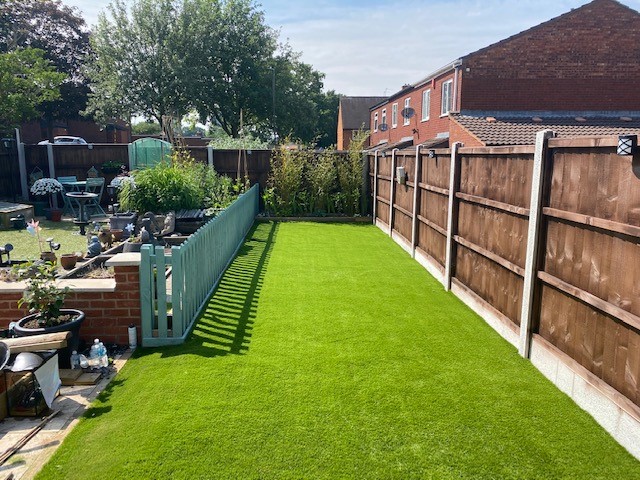 Artificial grass surface installed in a rectangular section of a backyard surrounded by fencing