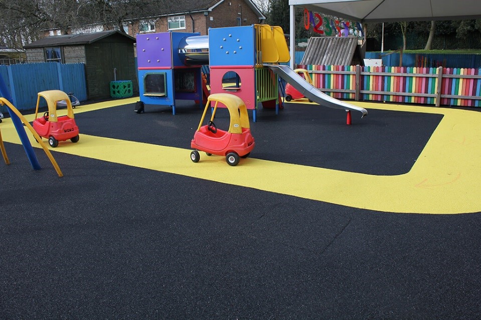 Vibrant yellow track around playground equipment with black safety surfacing. A racing track for children's car toys