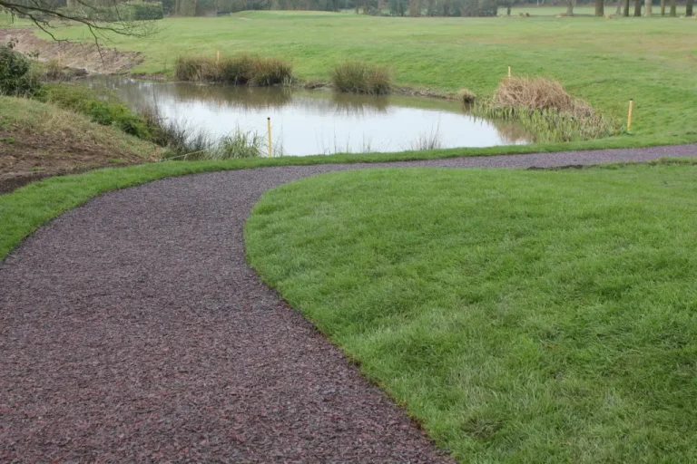 A golf pathway using our multi-coloured Jungle Mulch Rubber Mulch surface cover in a golf course, surrounded by grass and next to a pond