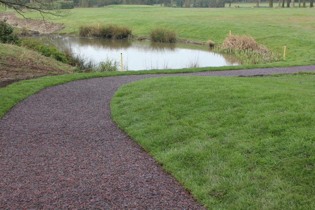 A golf pathway using our multi-coloured Jungle Mulch Rubber Mulch surface cover in a golf course, surrounded by grass and next to a pond