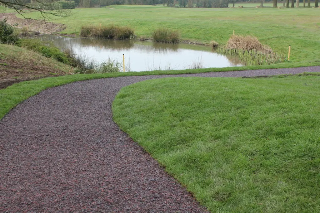 A golf pathway using our multi-coloured Jungle Mulch Rubber Mulch surface cover in a golf course, surrounded by grass and next to a pond