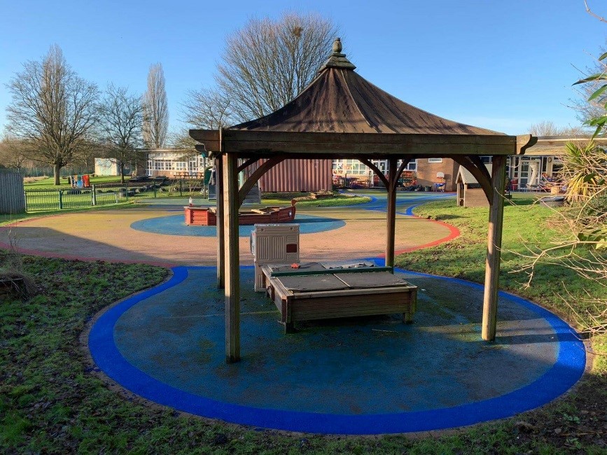 Playsmart’s rubber surfacing used on a playground in blue and sand-coloured rubber mulch colours in a circular pattern under a gazebo shelter