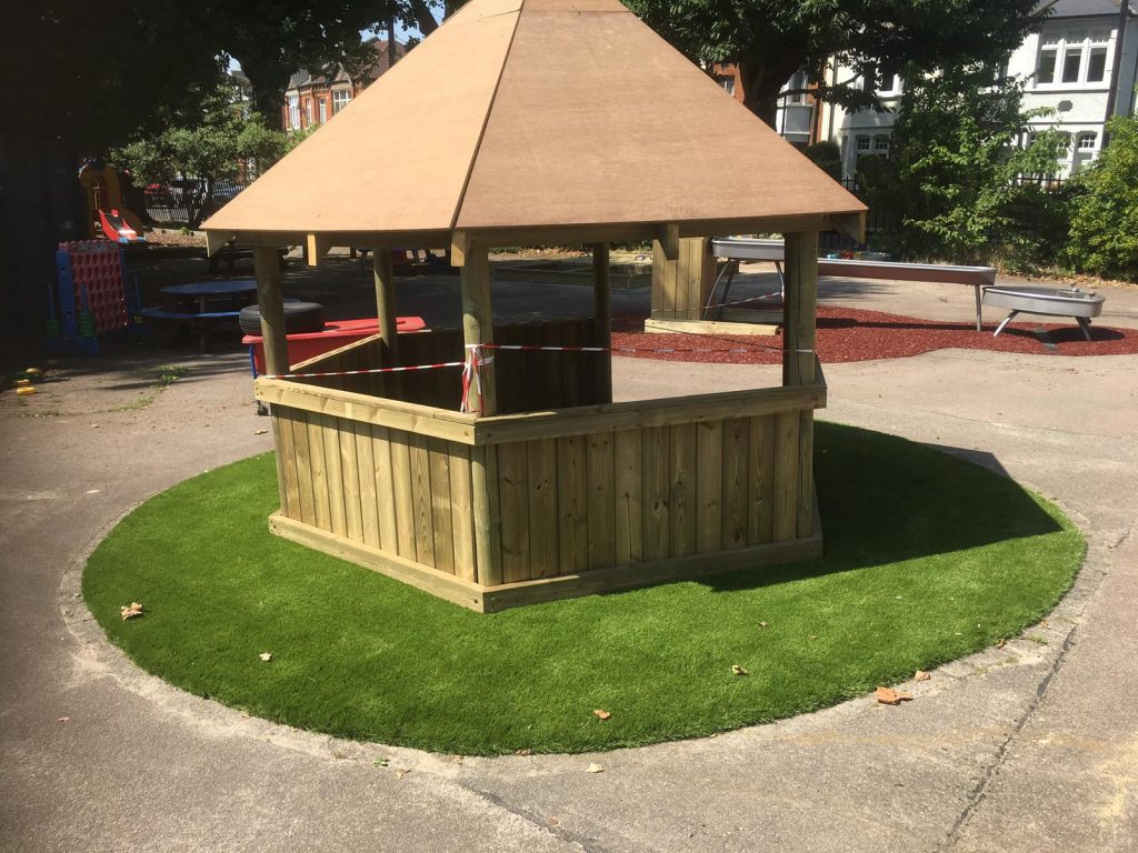 Green Frog Artificial Grass in a circle shape around a large wooden Wendy house gazebo play house.