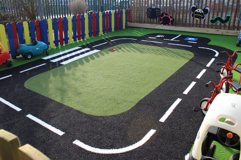 Image of Green Frog Artificial Grass used in a rectangular road track on a play area, with green artificial grass at the centre and black and white patterned artificial grass used for the road design.