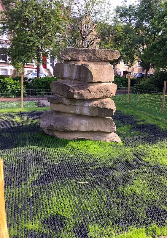 Rubber Grass mats with grass growing through the holes under a tall piles of rocks