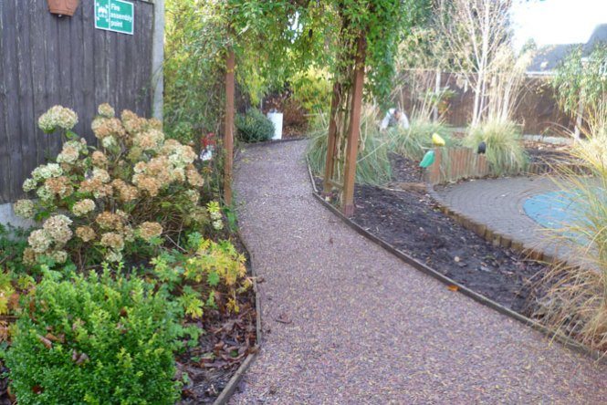 Playground rubber mulch path with green vegetation and wooden trellis arch