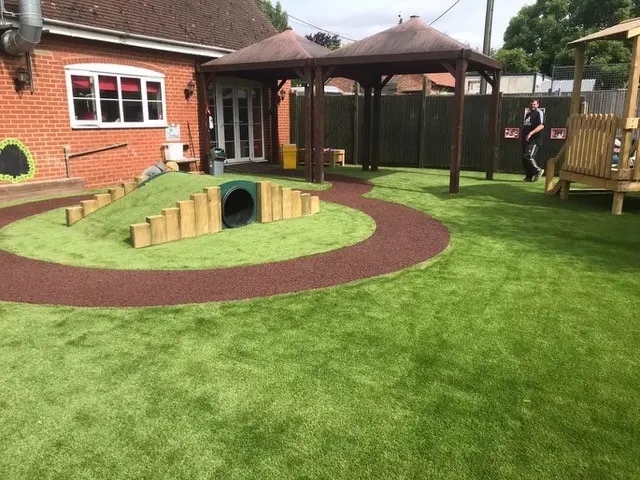Playground with multiple surfacing materials including a rubber mulch round pathway and artificial grass tunnel mound
