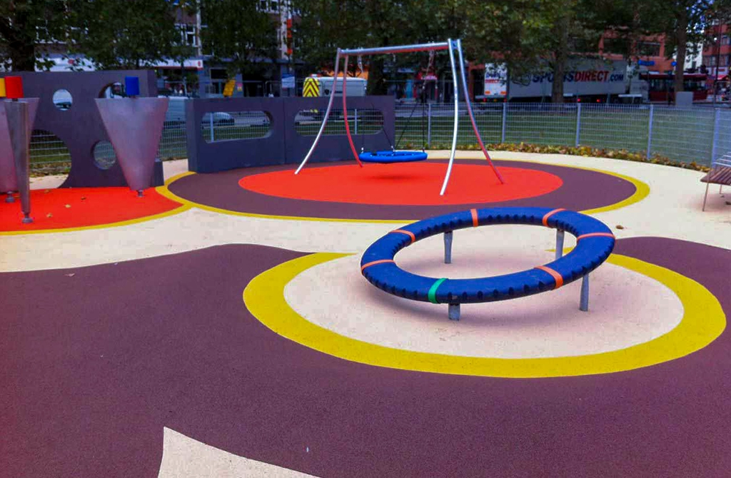 Wet Pour Rubber Playground with white base and purple, yellow, and red circle patterns around equipment