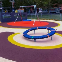 Wet Pour Rubber Playground with white base and purple, yellow, and red circle patterns around equipment