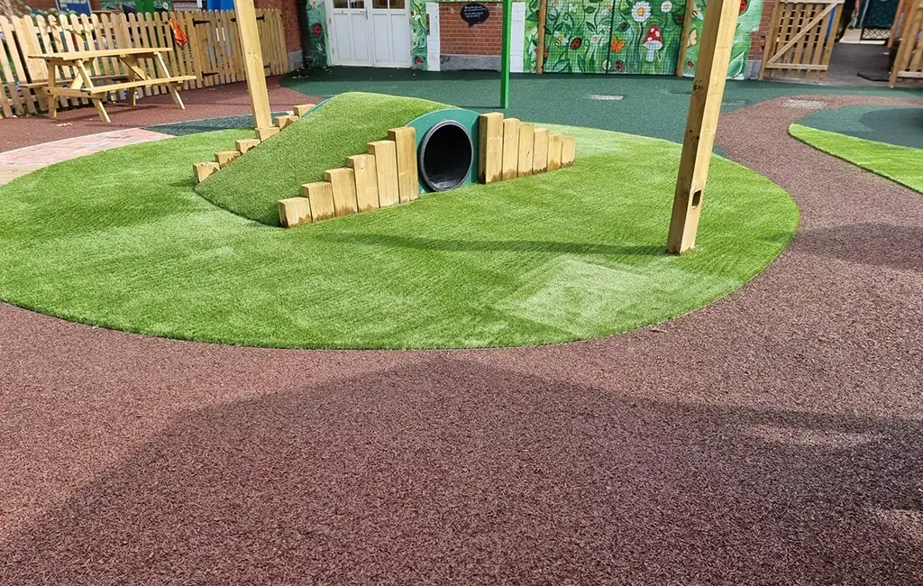 Playground with multiple surfacing materials including a rubber mulch round pathway and artificial grass tunnel mound
