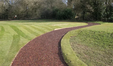 Striped artificial grass and red rubber mulch pathway in golf course