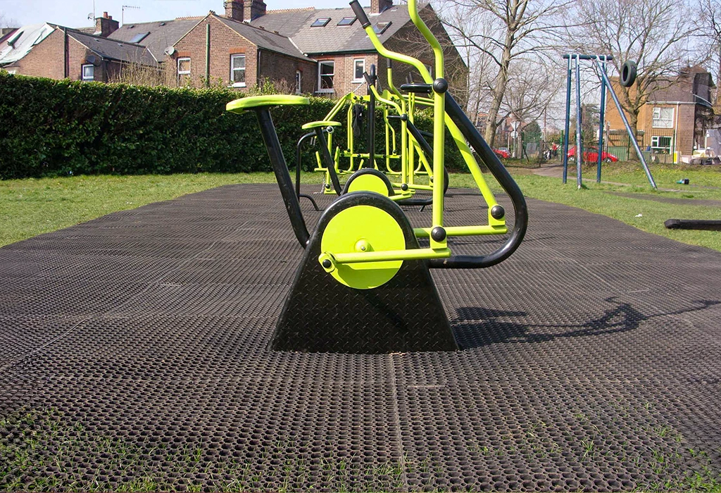 Rubber grass mats installed as safety surfacing underneath exercise bikes in outdoor gym