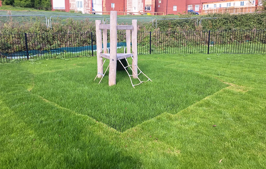Grass mats with grass grown through underneath small wooden playground climbing equipment