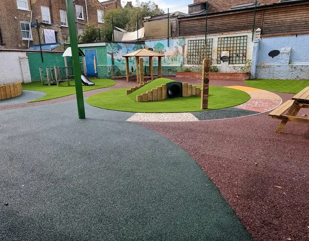 Red and green circular EPDM mulch path around artificial grass area with tunnel in playground