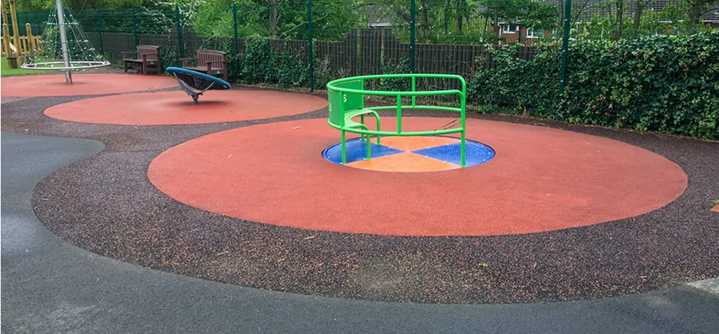 SmartPave playground installation with red mixed rubber surfaces around wheelchair accessible roundabout