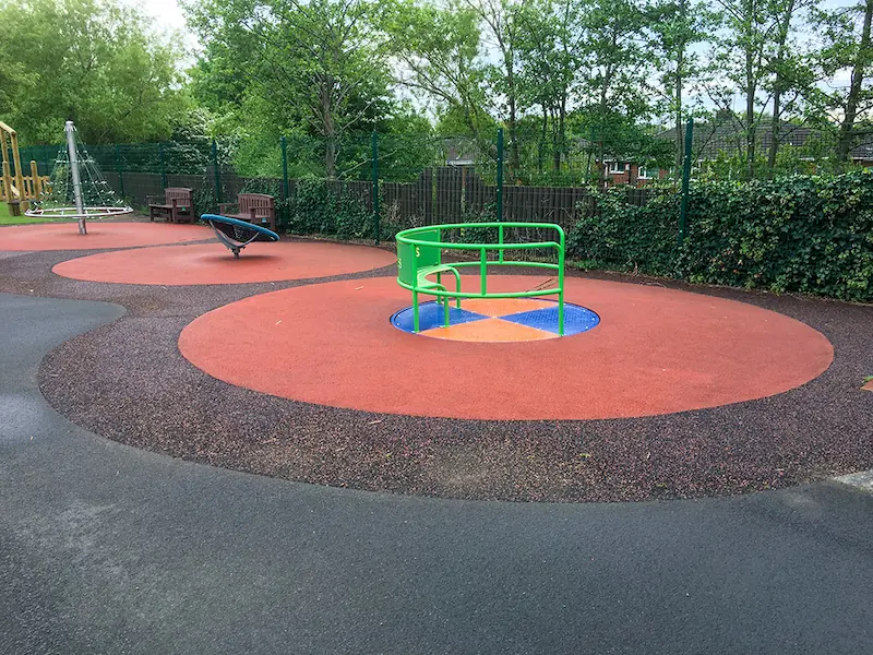 SmartPave playground installation with red mixed rubber surfaces around wheelchair accessible roundabout