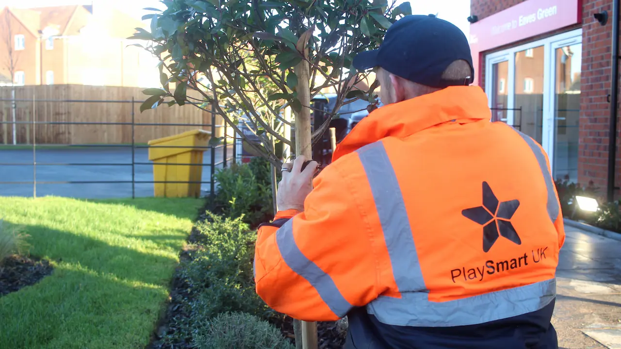 PlaySmart UK worker planting a tree in a housing estate garden