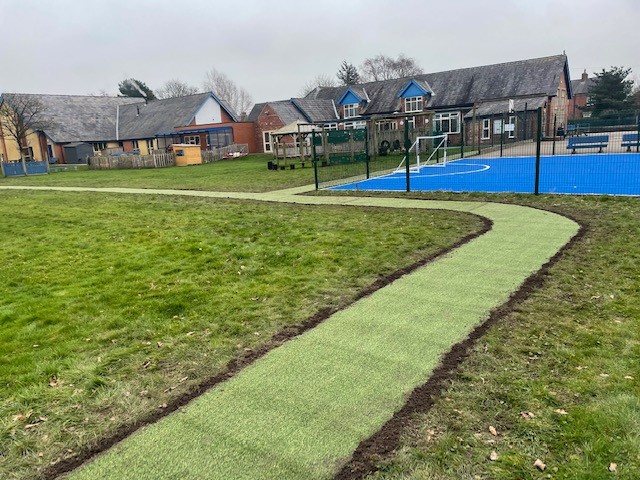 new artificial grass pathway leading to a school's blue MUGA court