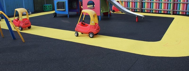 Vibrant yellow track around playground equipment with black safety surfacing. A racing track for children's car toys