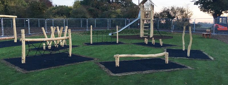 Black smart grass mats installed as safety surfacing underneath a range of wooden playground equipment