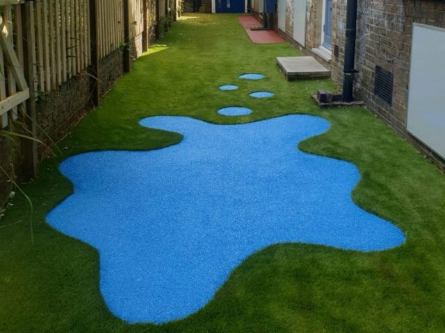 Artificial grass with bright blue wetpour surface shaped like splashed paint in the centre