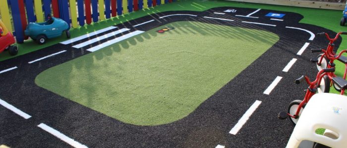 Green Frog Artificial Grass used in a rectangular road track on a play area, with green artificial grass at the centre and black and white patterned artificial grass used for the road design.