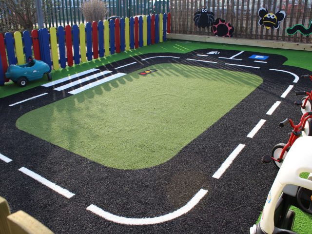 Green Frog Artificial Grass used in a rectangular road track on a play area, with green artificial grass at the centre and black and white patterned artificial grass used for the road design.