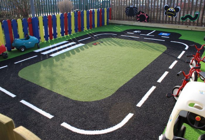 Green Frog Artificial Grass used in a rectangular road track on a play area, with green artificial grass at the centre and black and white patterned artificial grass used for the road design.