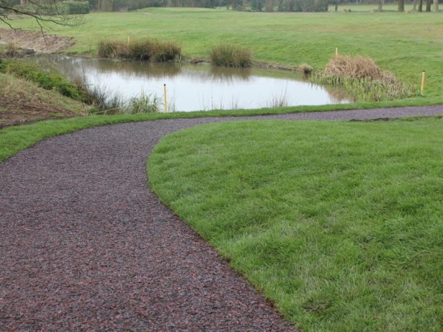 A golf pathway using our multi-coloured Jungle Mulch Rubber Mulch surface cover in a golf course, surrounded by grass and next to a pond