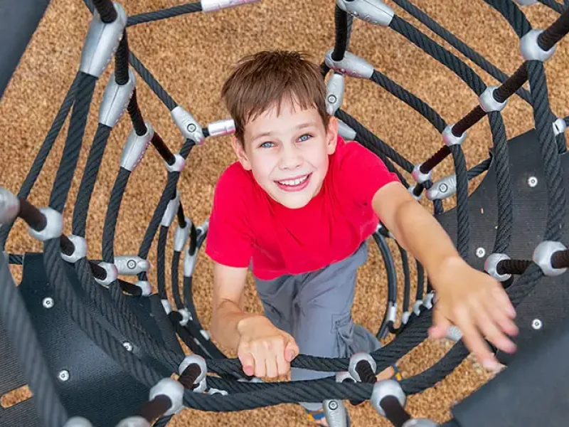 Child in playground climbing play equipment above safe Corkeen surfacing