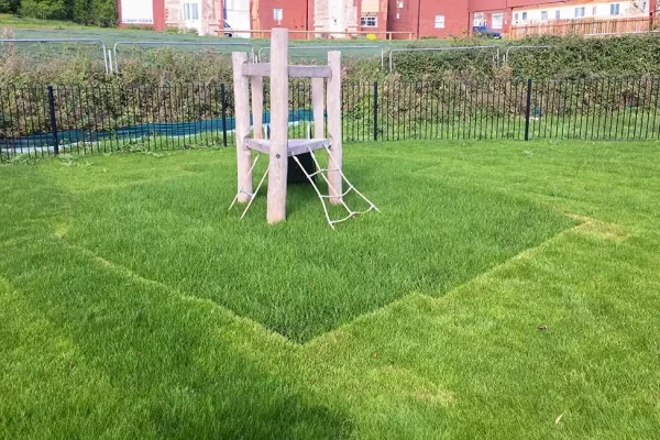 Grass mats with grass grown through underneath small wooden playground climbing equipment