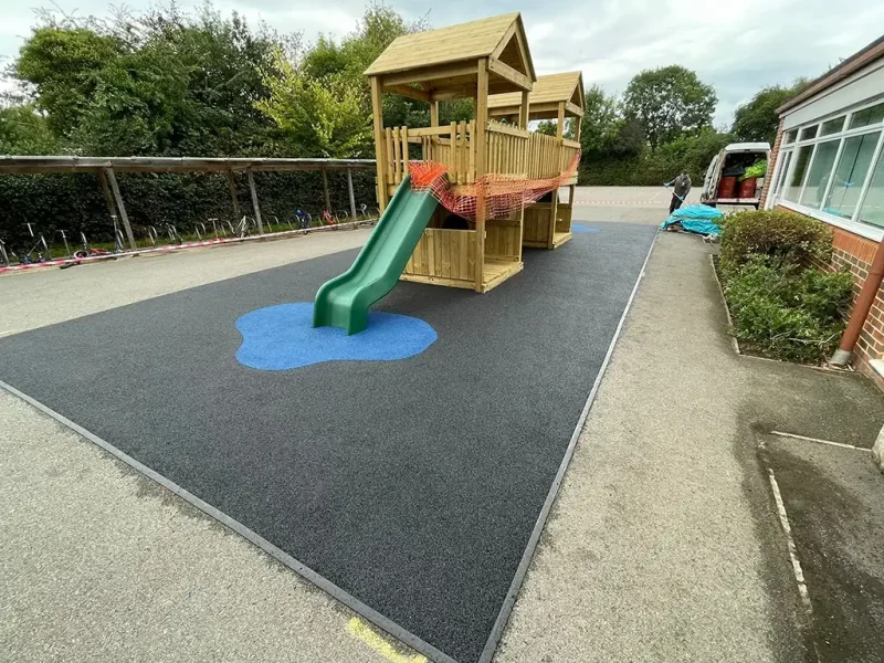 Black EPDM area with blue splash below multiplay structure with slide in school playground