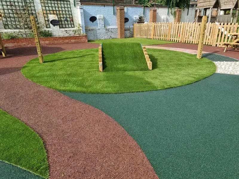 Red and green circular EPDM mulch path around artificial grass area with tunnel in playground