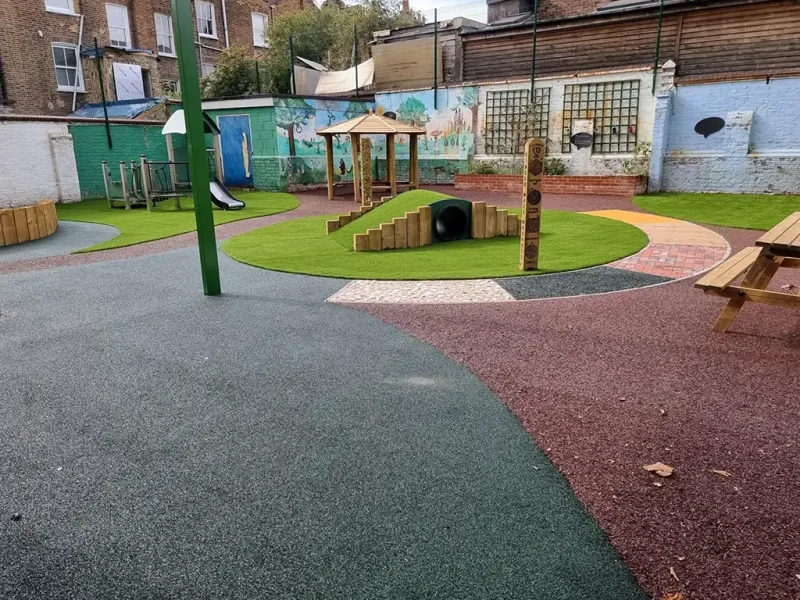 Red and black circular EPDM mulch path around artificial grass area with tunnel in playground