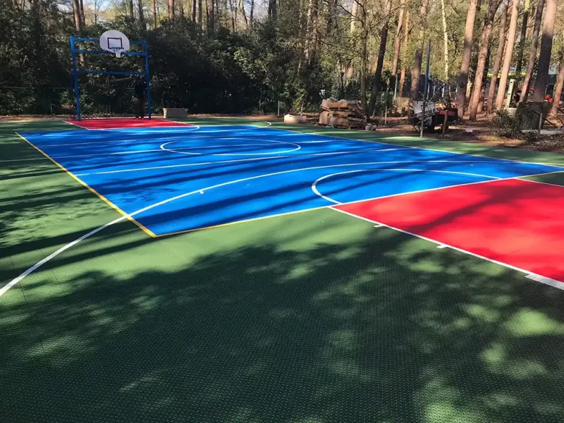 Blue FlexCourt basketball court in a wooded area with red scoring zones