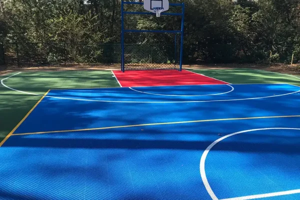 Blue FlexCourt basketball multi use games area MUGA court with red shooting zone in wooded area