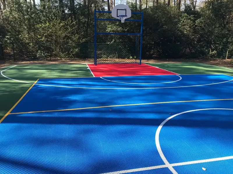 Blue FlexCourt basketball multi use games area MUGA court with red shooting zone in wooded area