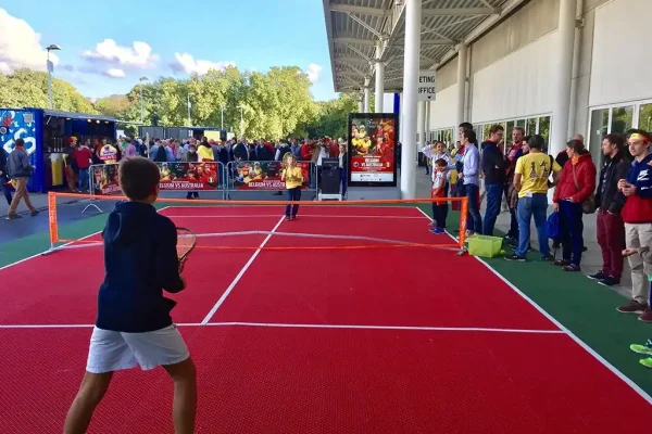A mini tennis court outside the Davis Cup with children playing on its bright red surface