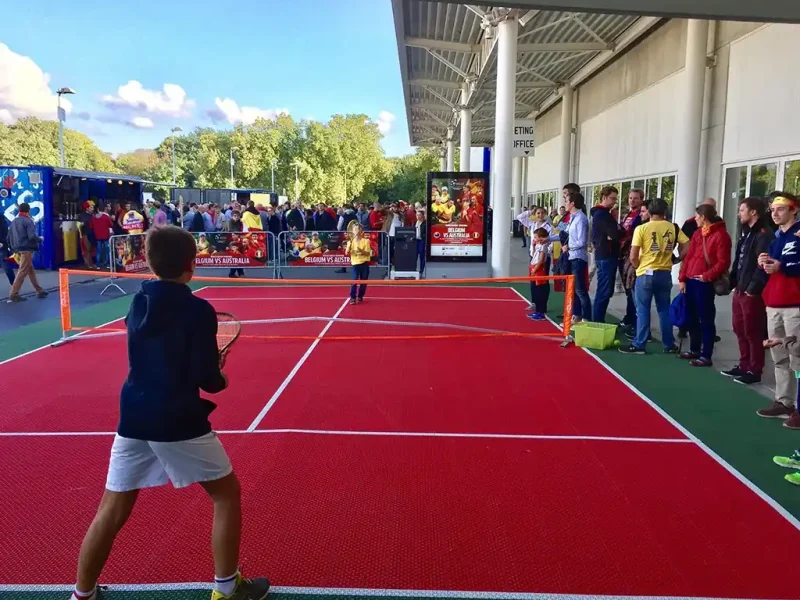 A mini tennis court outside the Davis Cup with children playing on its bright red surface