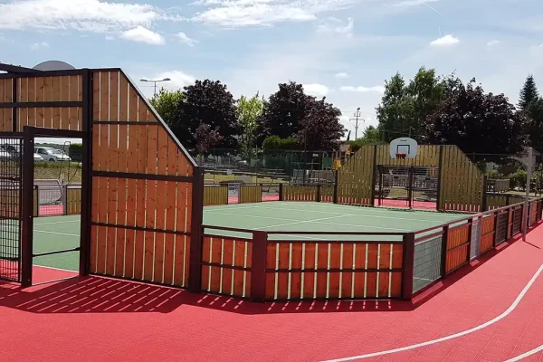 An enclosed green FlexCourt basketball court with red running track encircling it