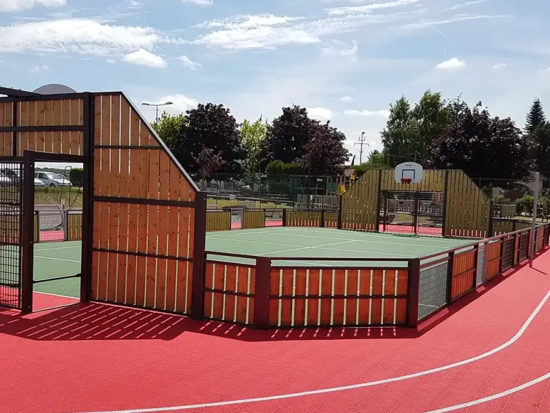 An enclosed green FlexCourt basketball court with read runnign track encircling it