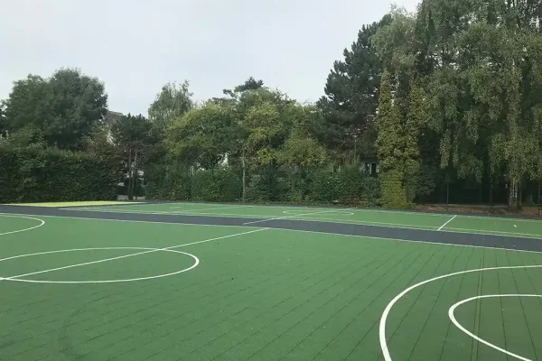 Multiple adjacent green FlexCourt netball courts in a wooded area