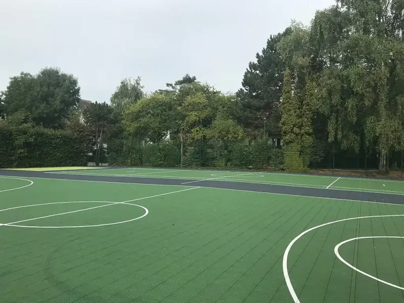 Multiple adjacent green FlexCourt netball courts in a wooded area