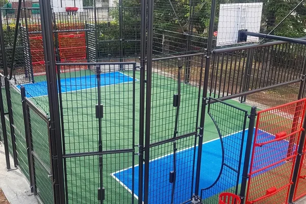 An enclosed mini multi use games area with green FlexCourt and blue scoring areas for football