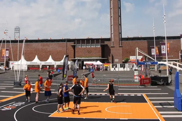 Mini black FlexCourt basketball area with orange scoring zone outside an Olympic stadium