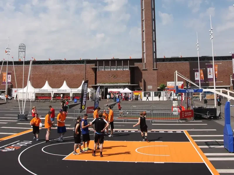 Mini black FlexCourt basketball area with orange scoring zone outside an Olympic stadium